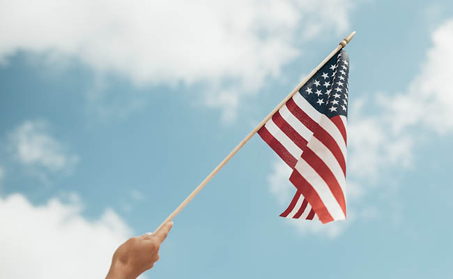 hand waving american flag in front of blue sky with clouds