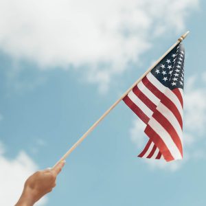 hand waving american flag against a blue sky background