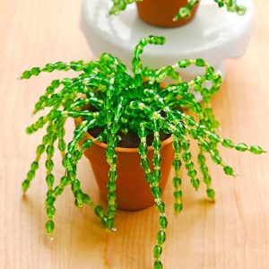 A small potted plant made of green beads on a wooden surface.