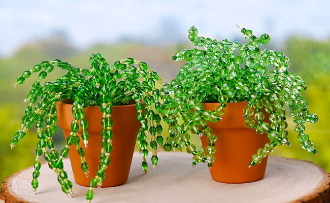 Two small potted plants made of green beads on a wooden surface.